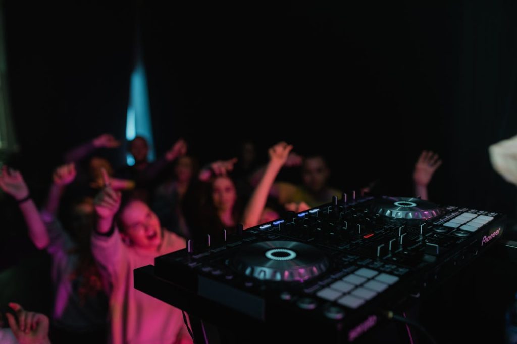 DJ mixer in focus as crowd dances energetically in club atmosphere.